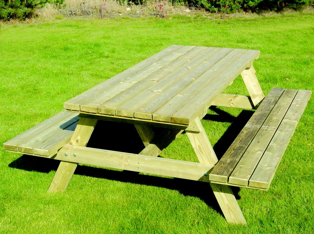 Drewniany stół piknikowy z ławkami, impregnowany na zielono, ustawiony na soczystej, zielonej trawie w słoneczny dzień.